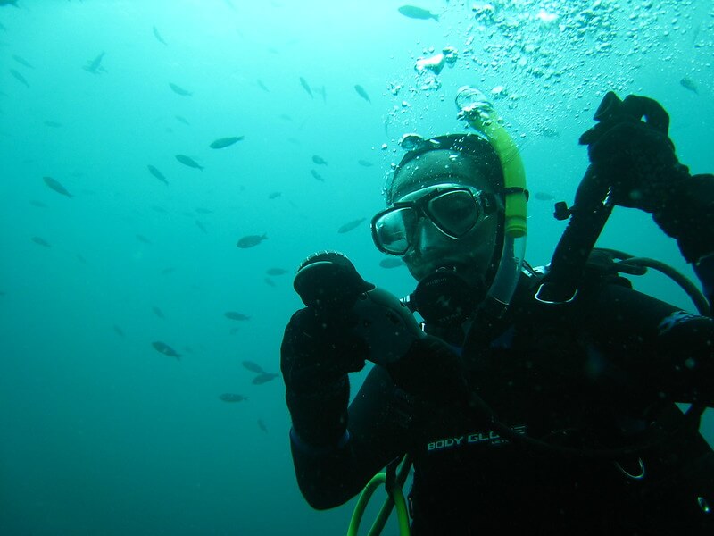 Das Bild zeigt eine Taucherin die Unterwasser Informationen von Ihrem Tauchcomputer für Anfänger abließt während Sie gerade den Schlauch Ihres BCD in der Hand hält. Sie ist von ein paar Fischen umgeben.