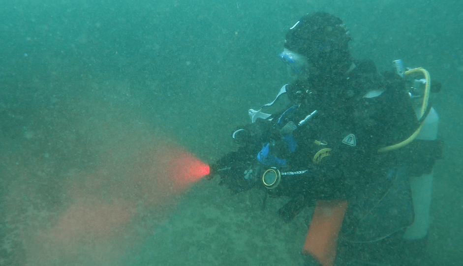 Taucher testet eine Tauchlampe mit Rotlicht Funktion bei mittelmäßiger Sicht unterwasser