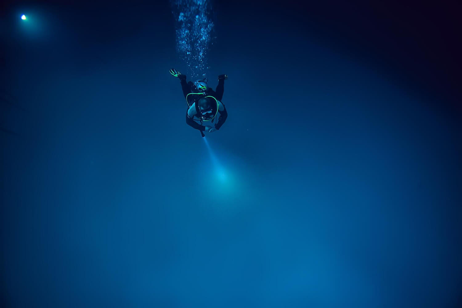 Taucher in dunklem Wasser leuchtet mit einer der besten Tauchlampen ins Blauwasser