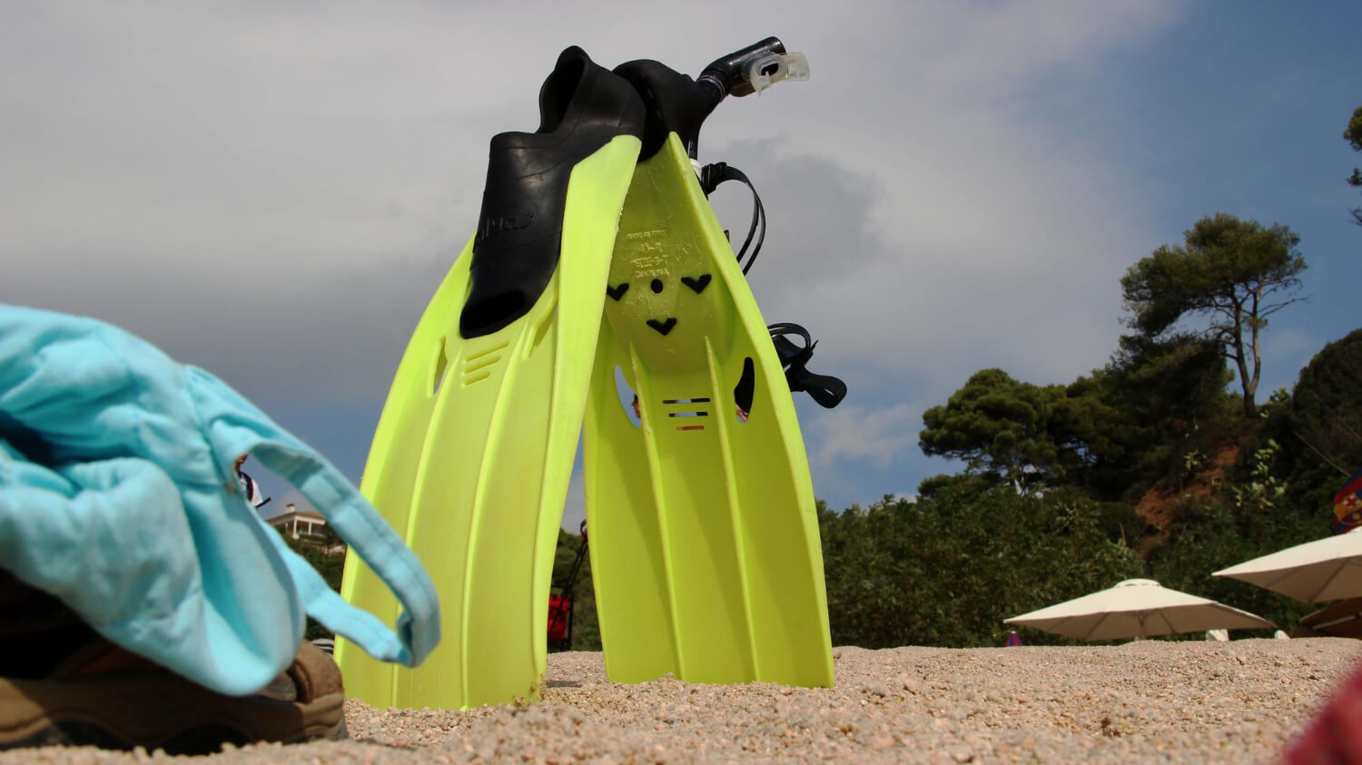 Zwei der besten Flossen für Schnorcheln stehen am Strand neben einer blauen Tasche