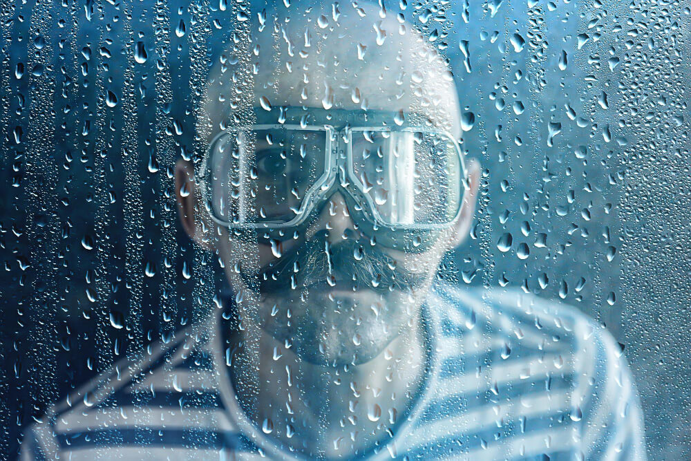 Mann mit Schnurrbart steht mit beschlagener Taucherbrille hinter einer mit Kondenswasser benetztem Glasscheibe