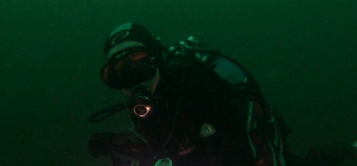 taucher test eine schwarz, silberne kopfhaube in dunklerem Wasser