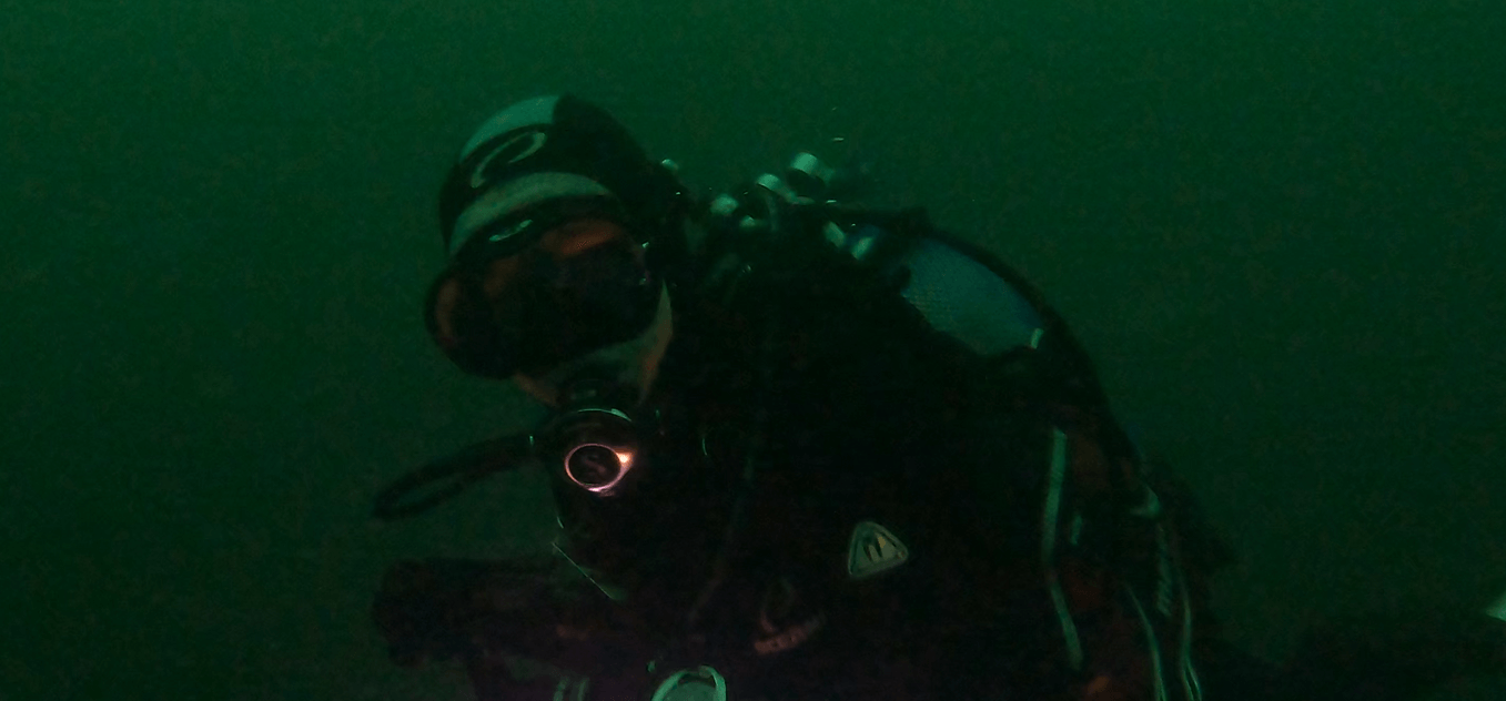 taucher test eine schwarz, silberne kopfhaube in dunklerem Wasser