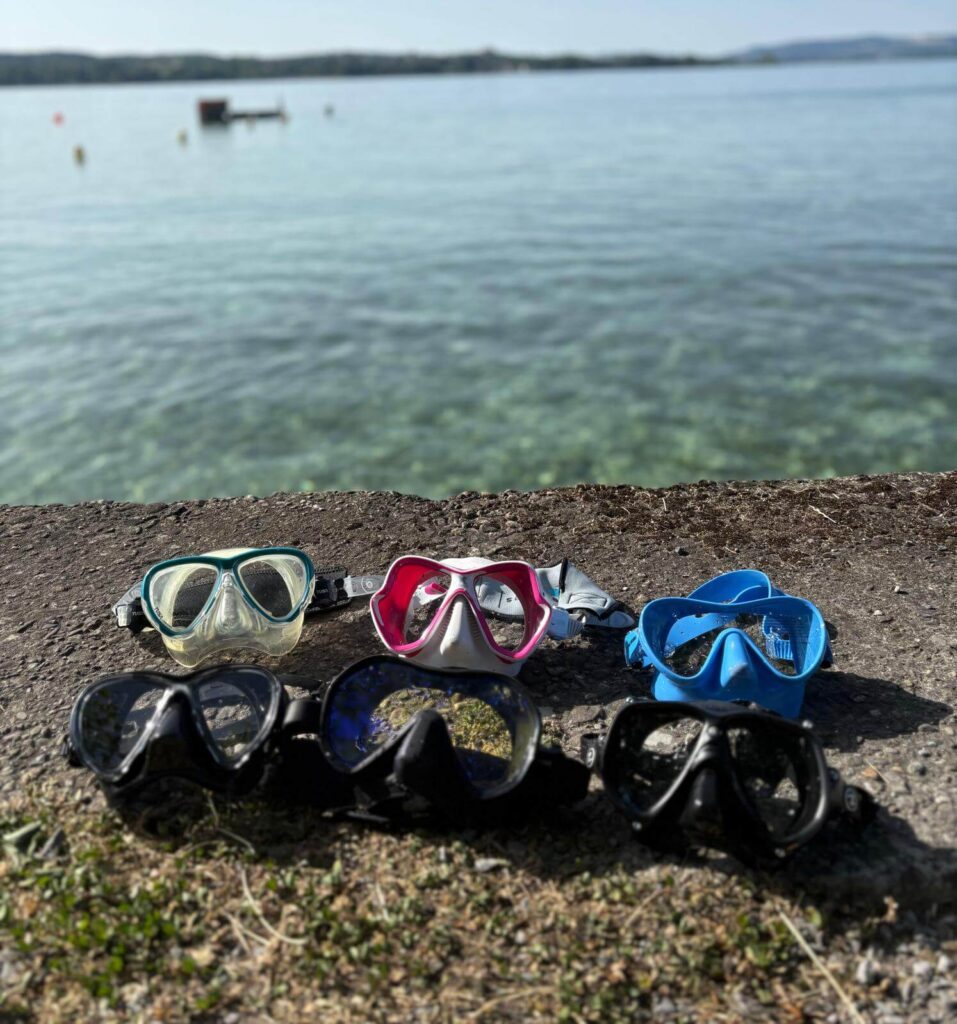 Sechs Tauchmasken im Test – aufgenommen mit Bodensee im Hintergrund.