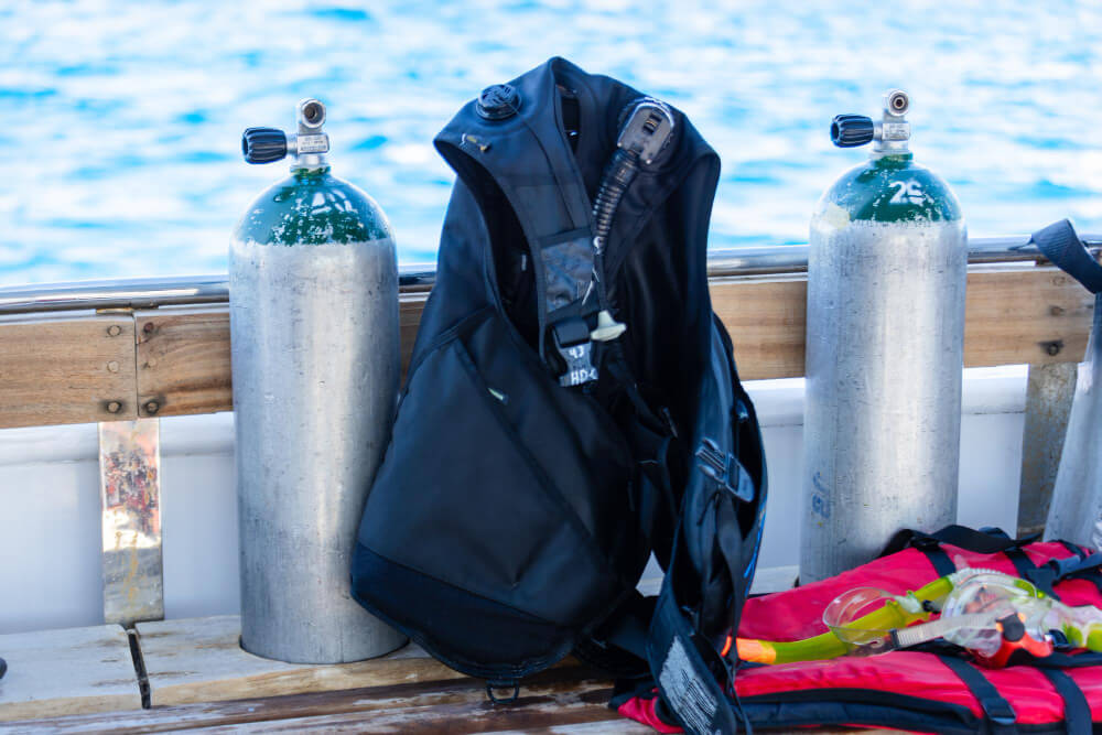 Schwarzes Tarierjacket steht neben Tauchflaschen auf einem Boot