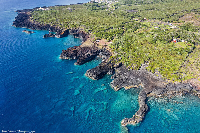 Luftaufnahme der Küste von Ilha do Pico mit dem Vulkan Pico im Hintergrund und klaren Küstengewässern