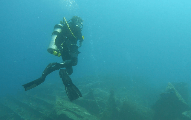 Taucher nimmt aufrechte Wasserlage ein und schaut Schatten eines Hais im Blauwasser an