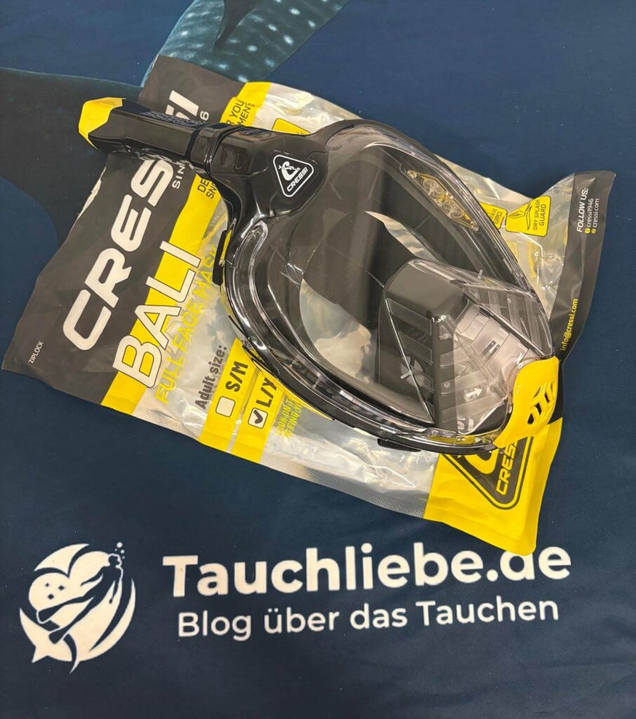 Schwarze Schnorchelmaske mit Plastikverpackung auf Handtuch mit Tauchliebe Logo