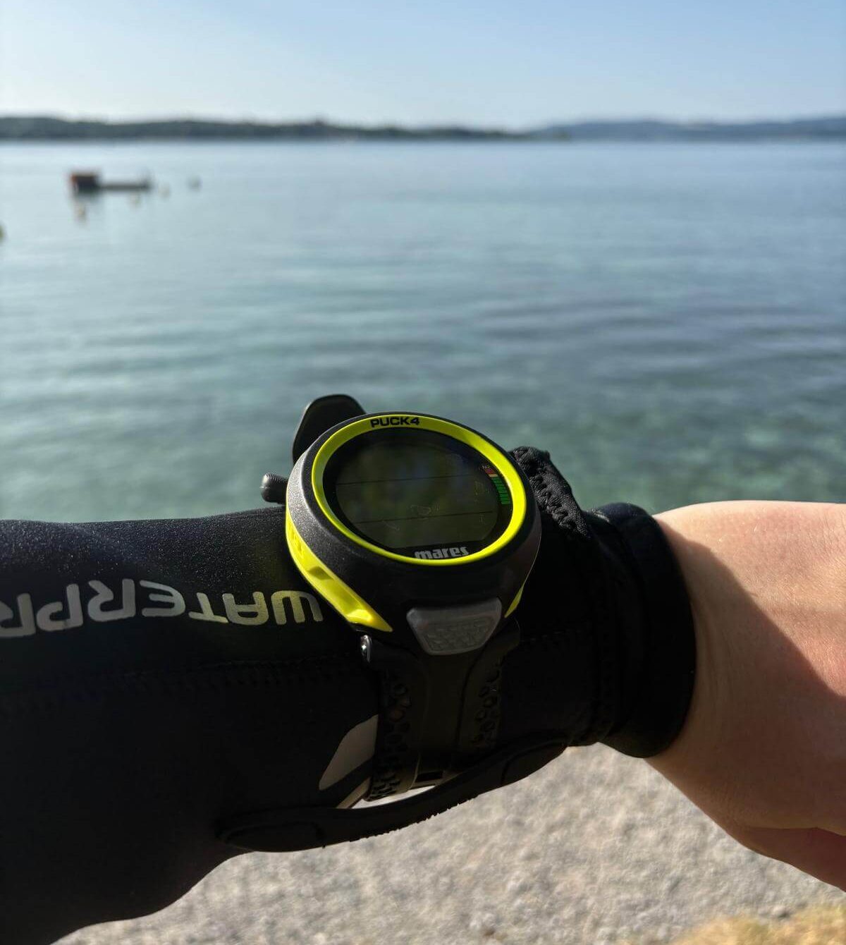 Mares Puck 4 Tauchcomputer am Arm getragen vor See im Hintergrund