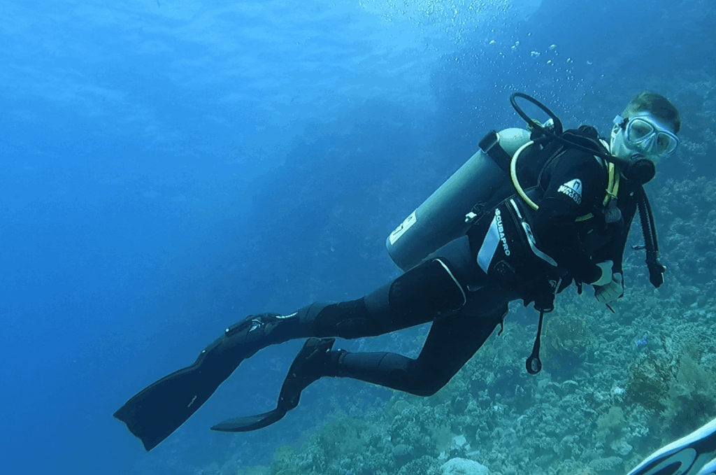 Junger taucher testet den Waterproof W7 Tauchanzug vor einem großen Korallenriff