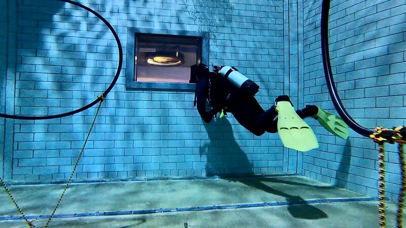 Taucher unterwasser vor einem Sichtfenster nach draußen aus dem Pool