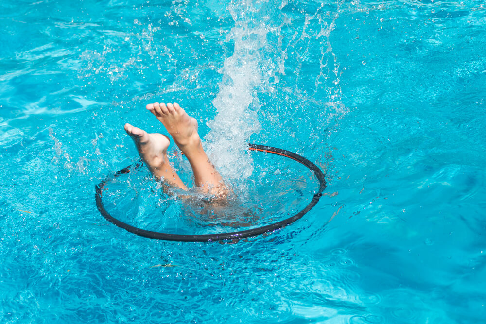 Fuße schauen aus dem Wasser heraus während eines Sprungs durch großen Ring an Wasseroberfläche