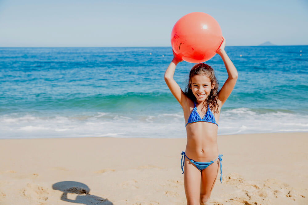 Kleines Mädchen mit Wasserball am Strand