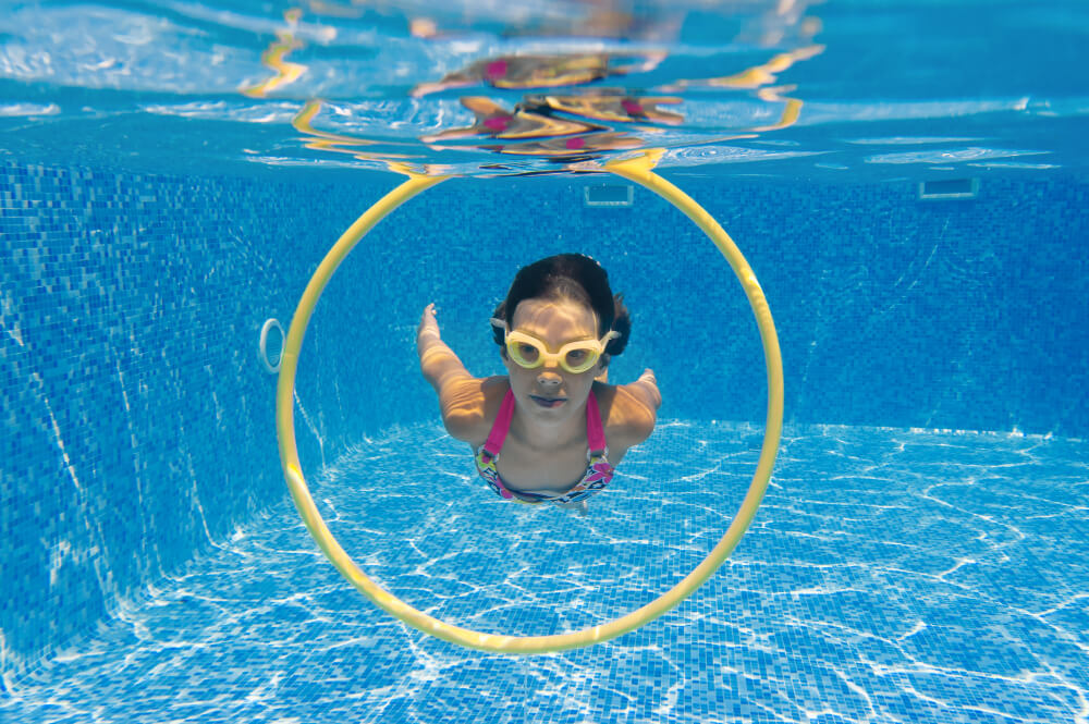 Mädchen mit Schwimmbrille taucht durch einen gelben Ring