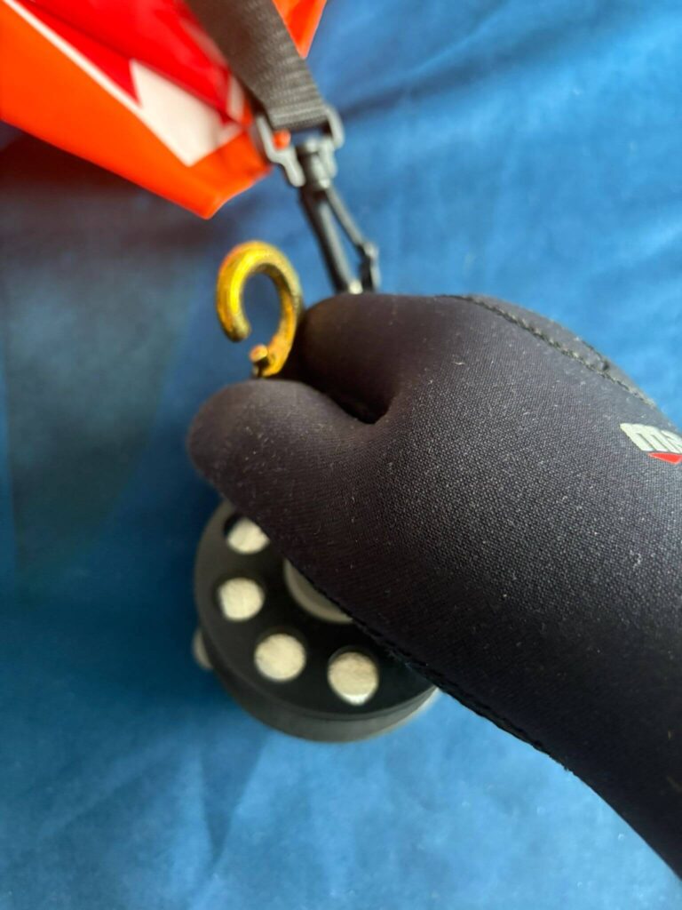 Beweglichkeitstest Tauchhandschuhen beim Öffnen eines Karabiners am Bojen-Reel an Land