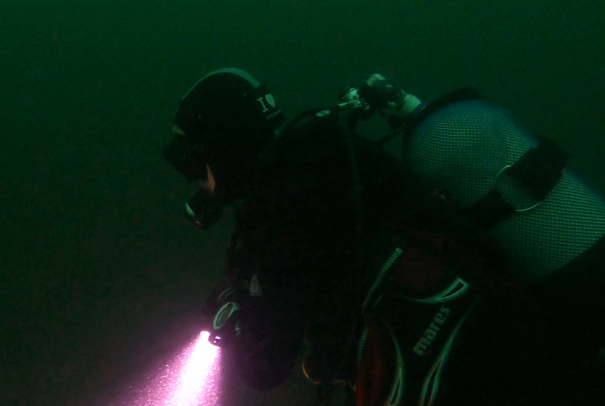 Taucher Unterwasser von der seite mit Tauchlampe und Atemregler von der Seite - 