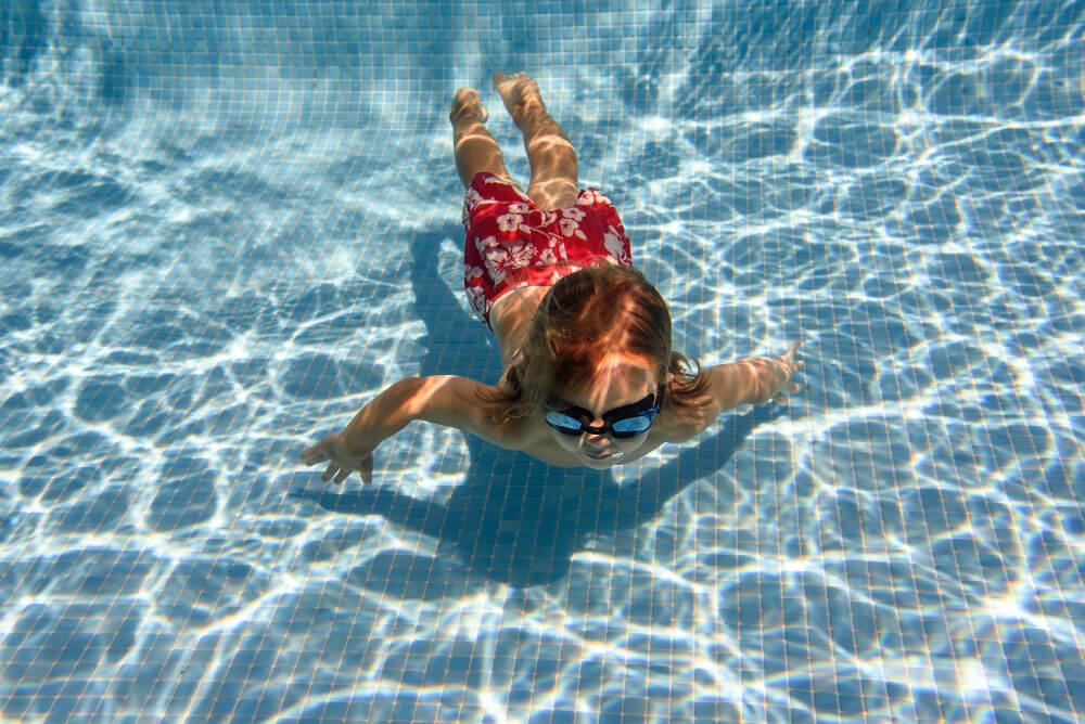 Kind mit rotes Badehose sucht Unterwasser am Boden eines Pools nach Tauchringen