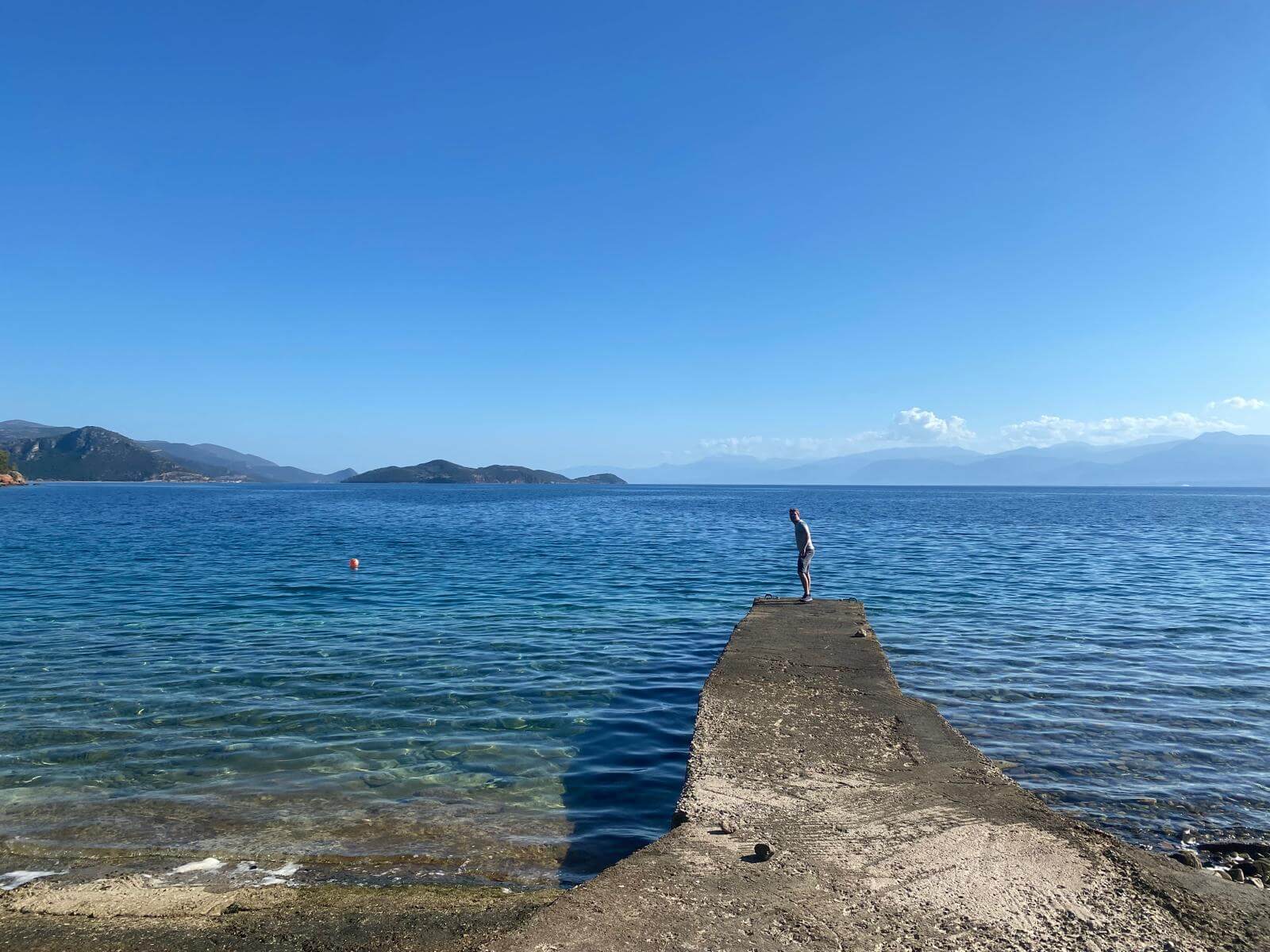 Mann steht an einem Steg aus Stein im Meer von Griechenland und schaut nach Haien im Wasser