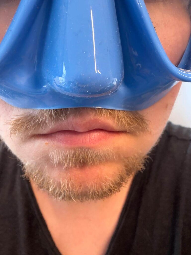 Taucher trägt blaue Tauchmaske über Oberlippenbart mit sichtbarer Lücke dazwischen.