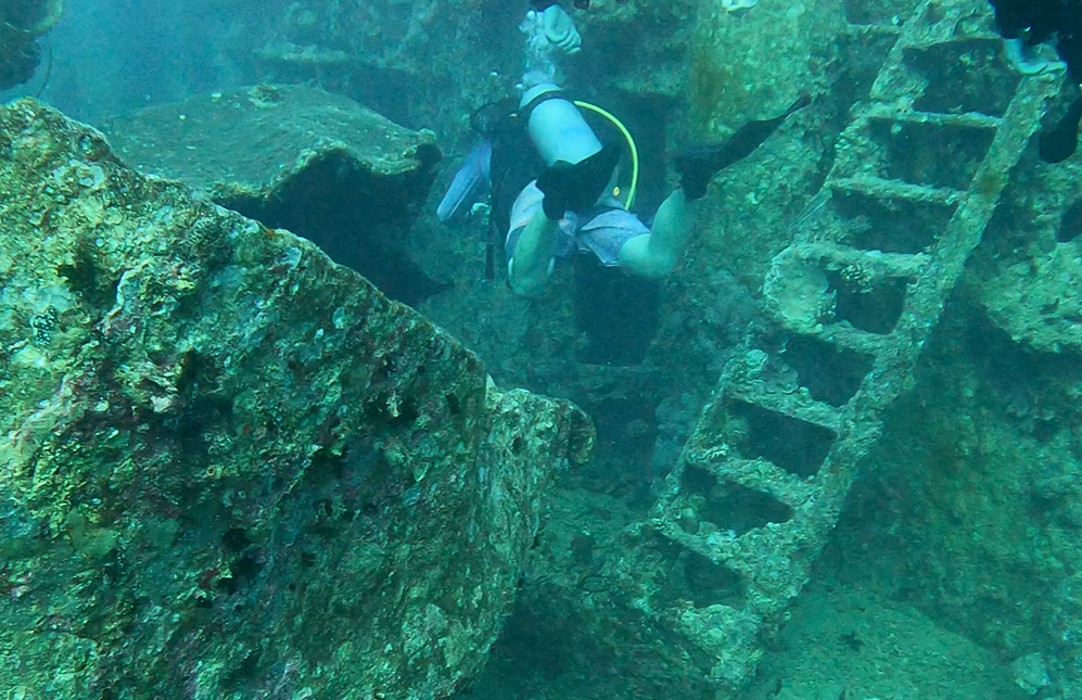 Taucher schwebt zwischen einem Schiffswrack neben einer Leiter
