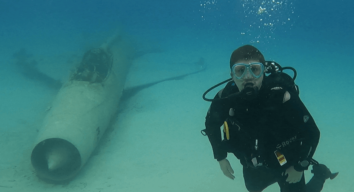 Taucher neben Mig Flugzeugwrack trägt Mares Rover 2. Stufe im Mund