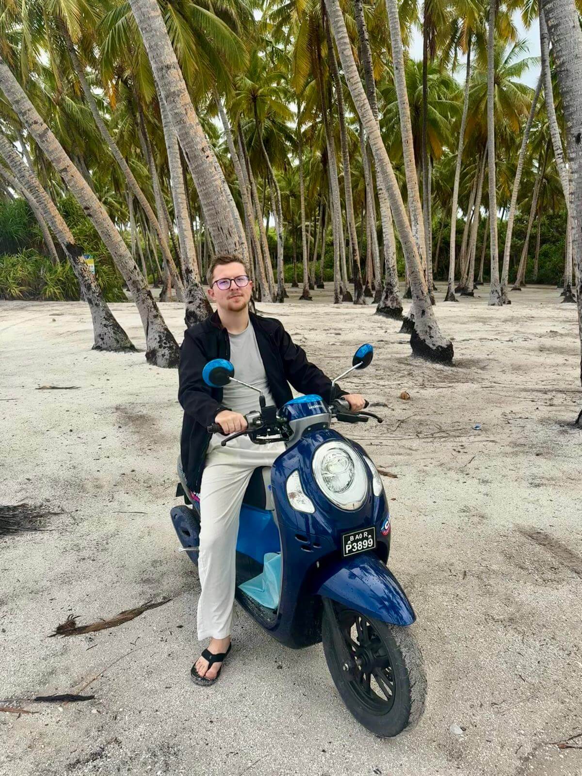 Marlon der Autor von Tauchliebe fährt einen Motorroller unter Palmen auf den Malediven am Strand von Fuvahmulah