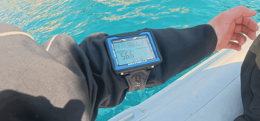 Taucher trägt Tauchcomputer am Arm auf einem Boot mit Wasser im Hintergrund
