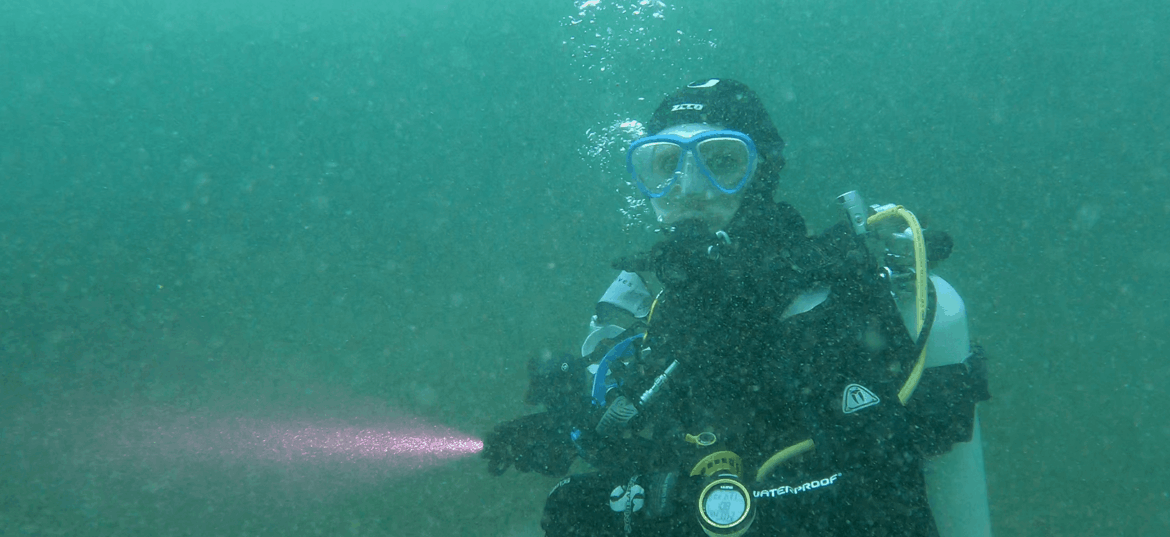 Taucher unter Wasser mit Tauchlampe in der Hand während eines Tauchgangs