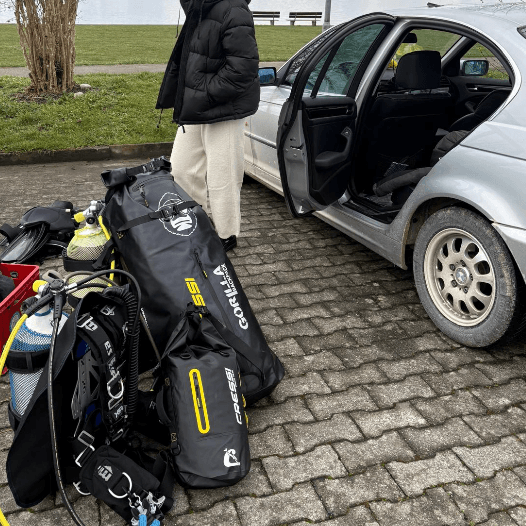 Vollständige Tauchausrüstung liegt am Seeufer neben Rucksack an einem Auto